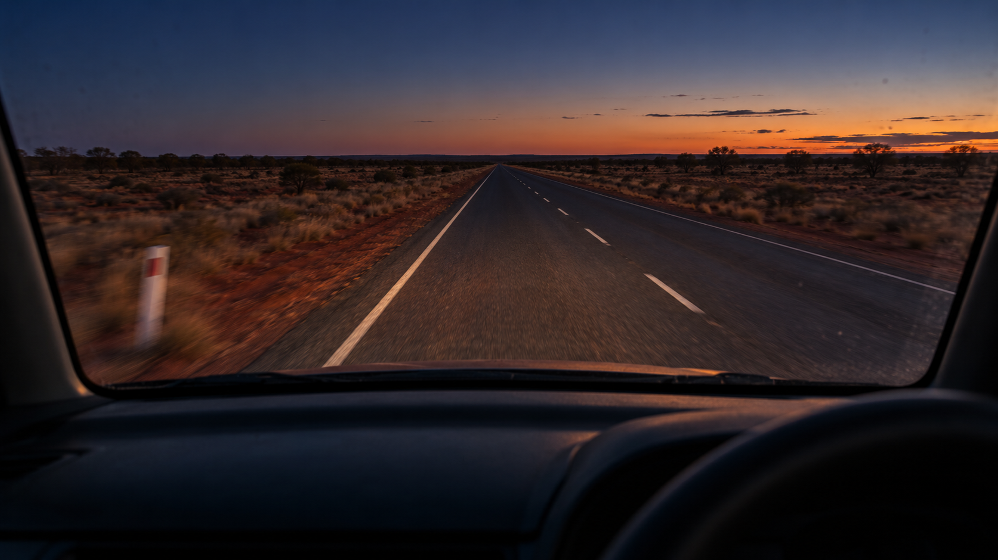 Editorial image: a remote road at dusk seen through a windscreen. No text in the artwork.