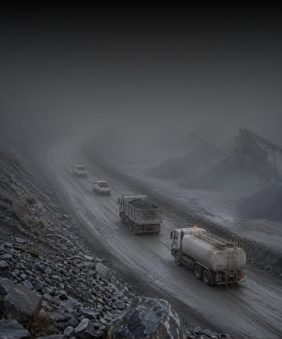 Photograph: a mixed fleet on a working site at first light. Dark and cool, room at the top, no text in the artwork.