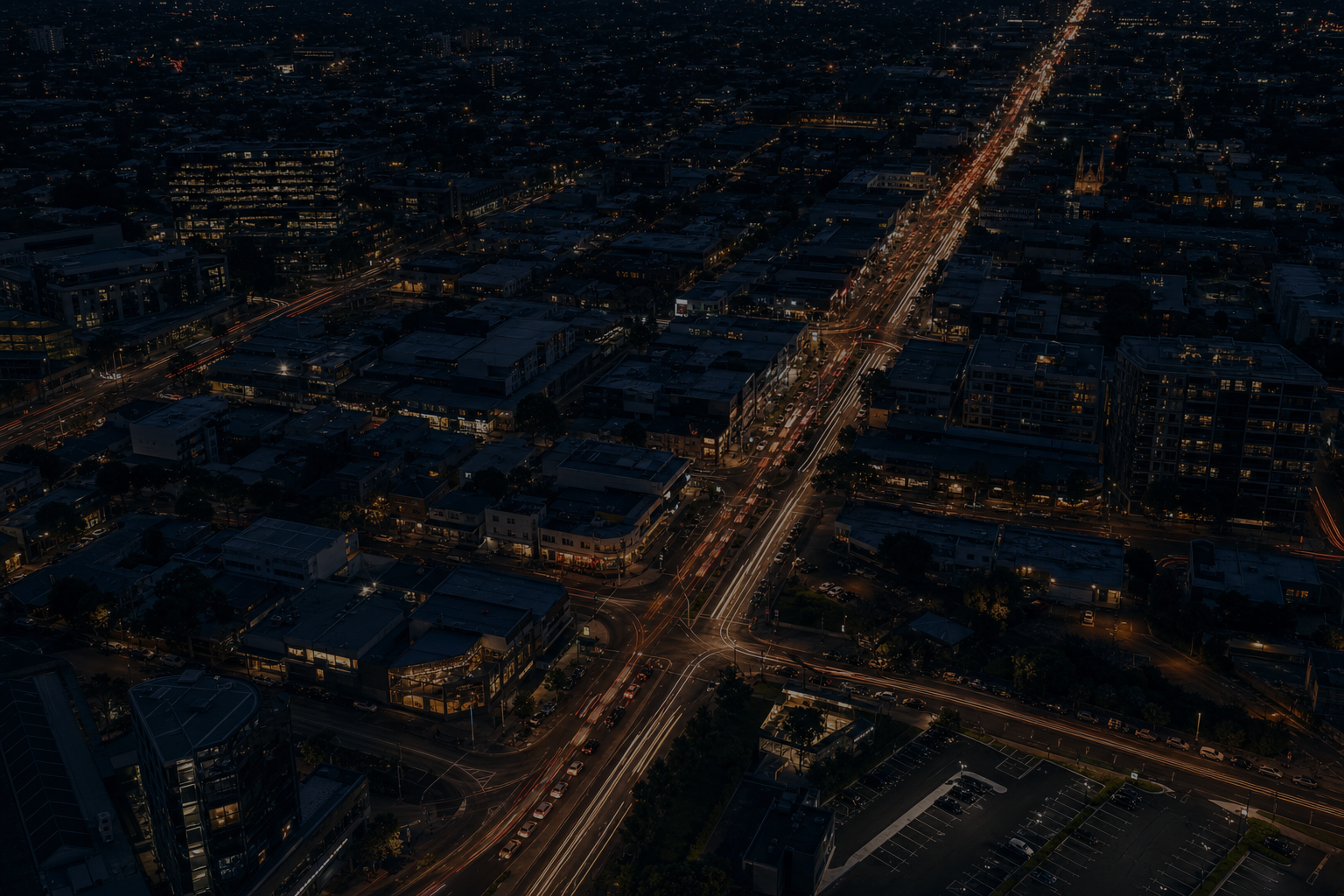 Full-bleed scene, edge to edge: a city arterial from height at dusk, headlight trails running through it, dark and cool so the headline and the accordion read over it. No text in the artwork. 2400x1400.