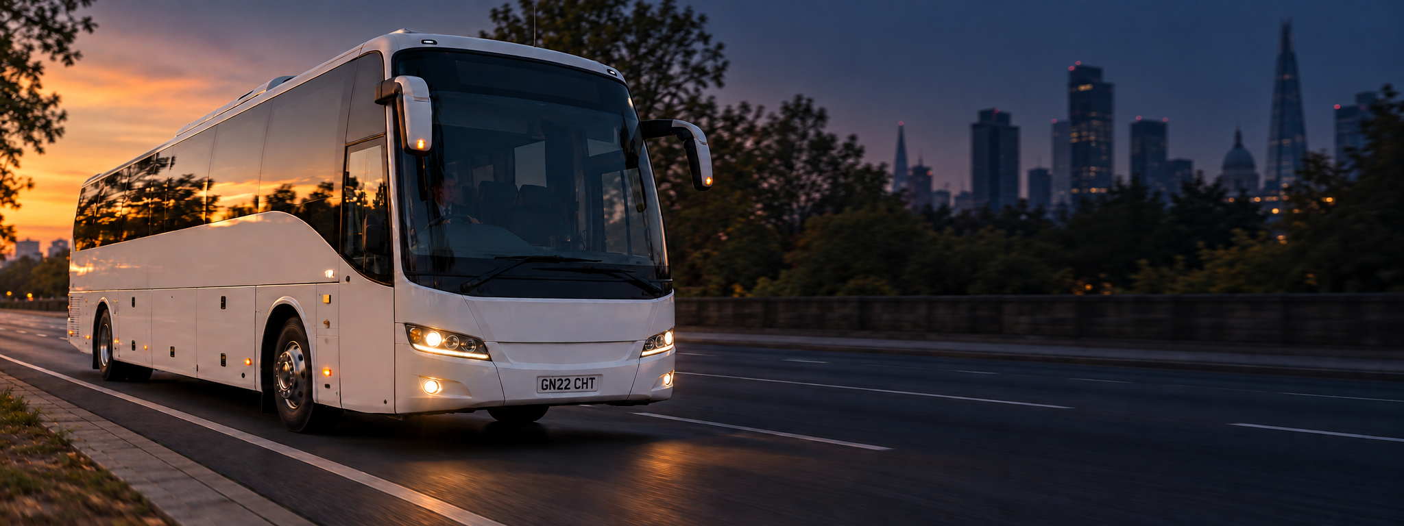 A coach on an arterial road at golden hour, shot from the front three-quarter, city behind it. Dark and cool enough for a panel to sit over the right third. No text in the artwork. 2400x900.