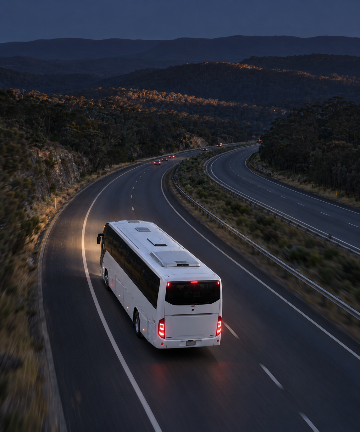 Photograph: a coach on a highway at dusk, shot from height. Dark and cool, room at the top, no text in the artwork.