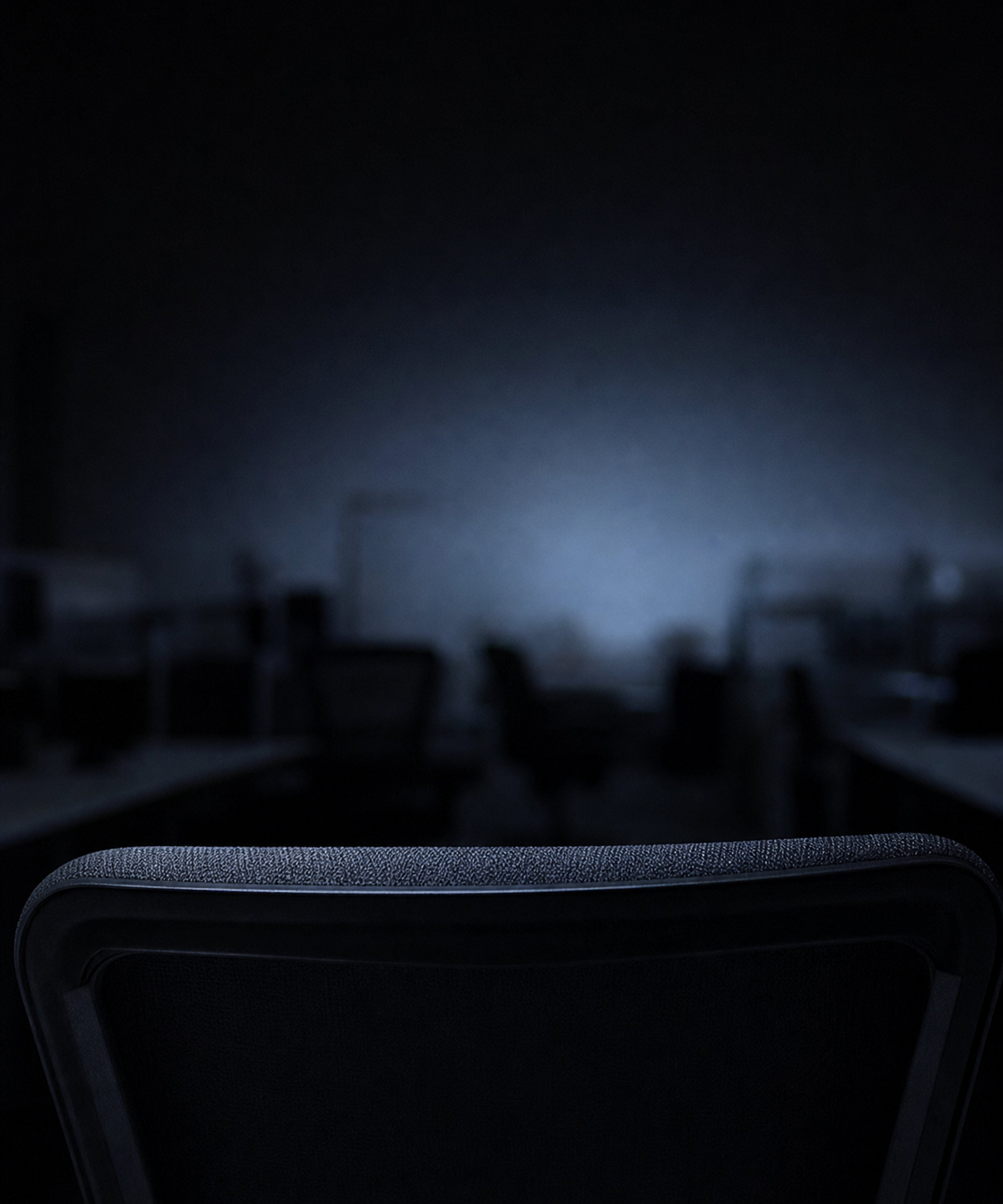 Photograph: a quiet office detail at night, screen glow only. Dark and cool, room at the top, no text in the artwork.