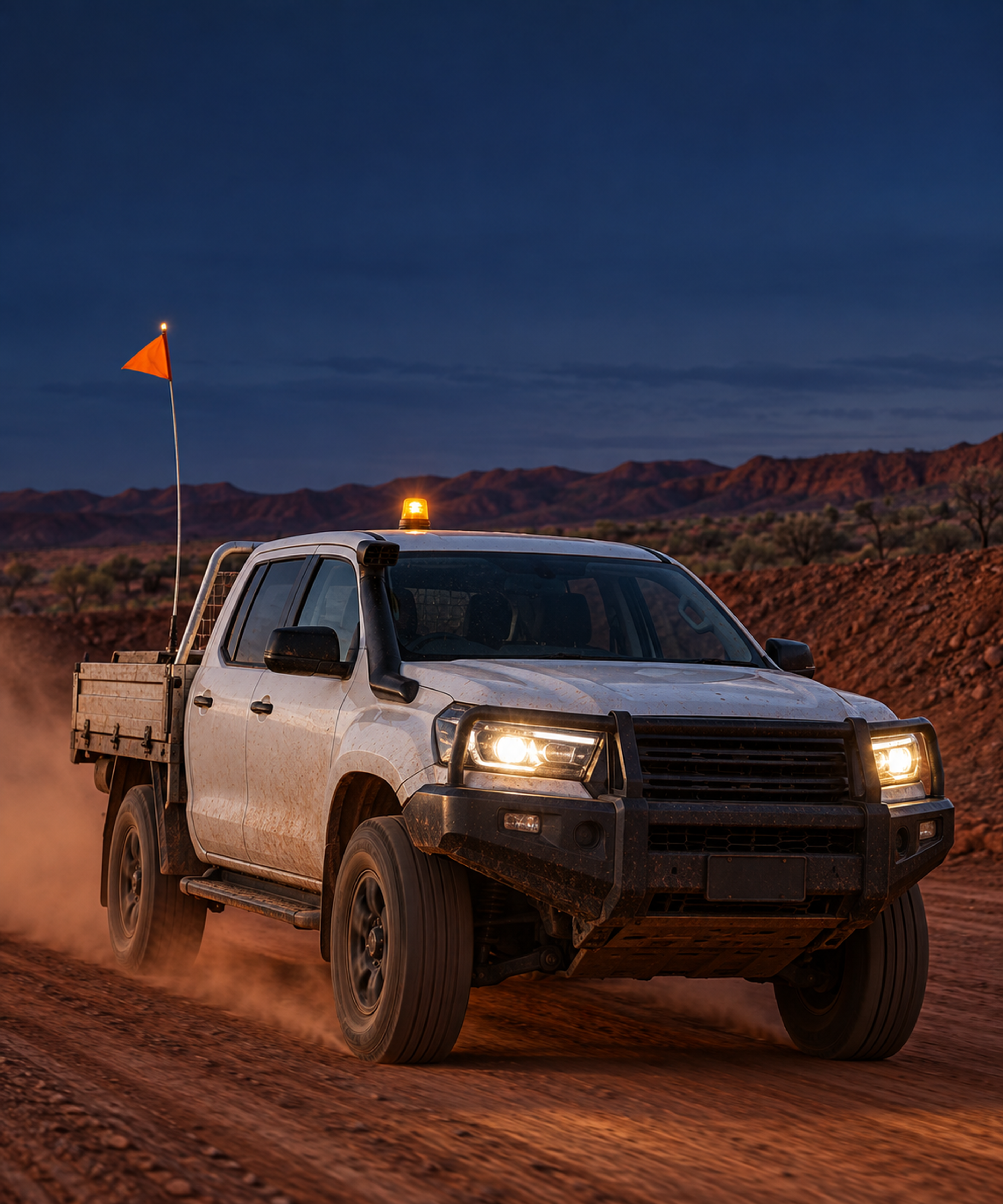 Photograph: a light vehicle on a haul road at first light. Dark and cool, room at the top, no text in the artwork.