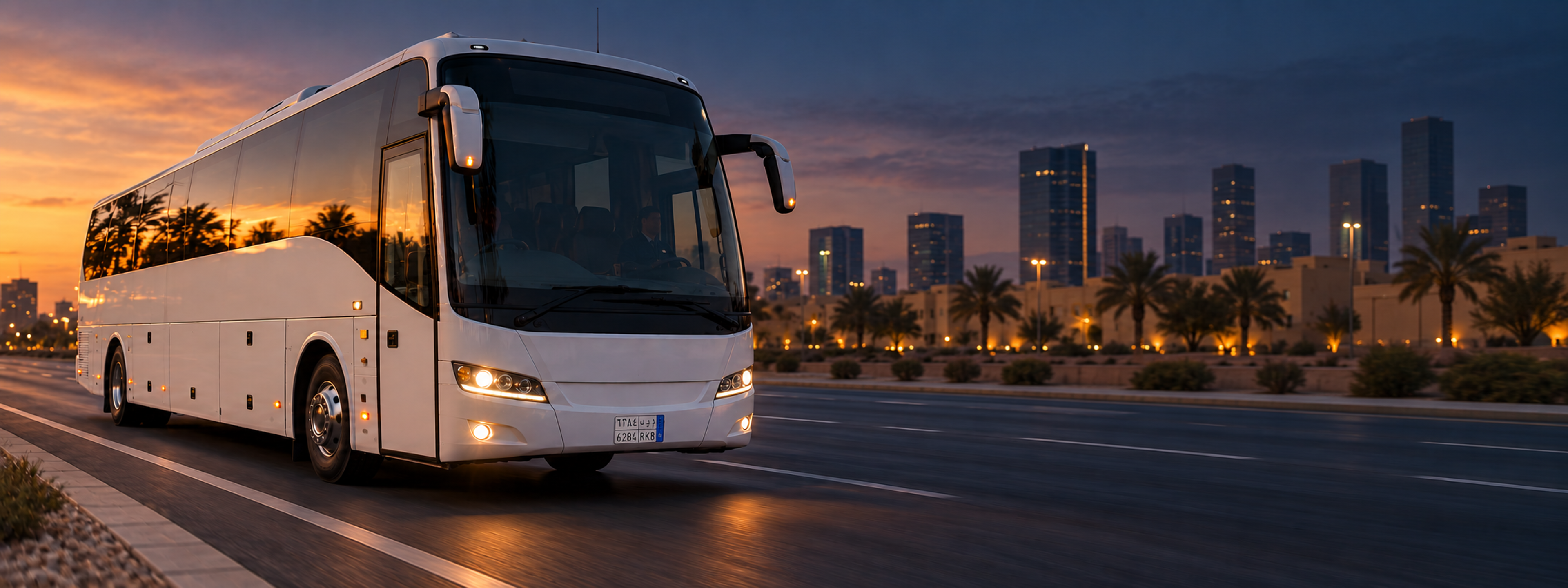A coach on an arterial road at golden hour, shot from the front three-quarter, city behind it. Dark and cool enough for a panel to sit over the right third. No text in the artwork. 2400x900.