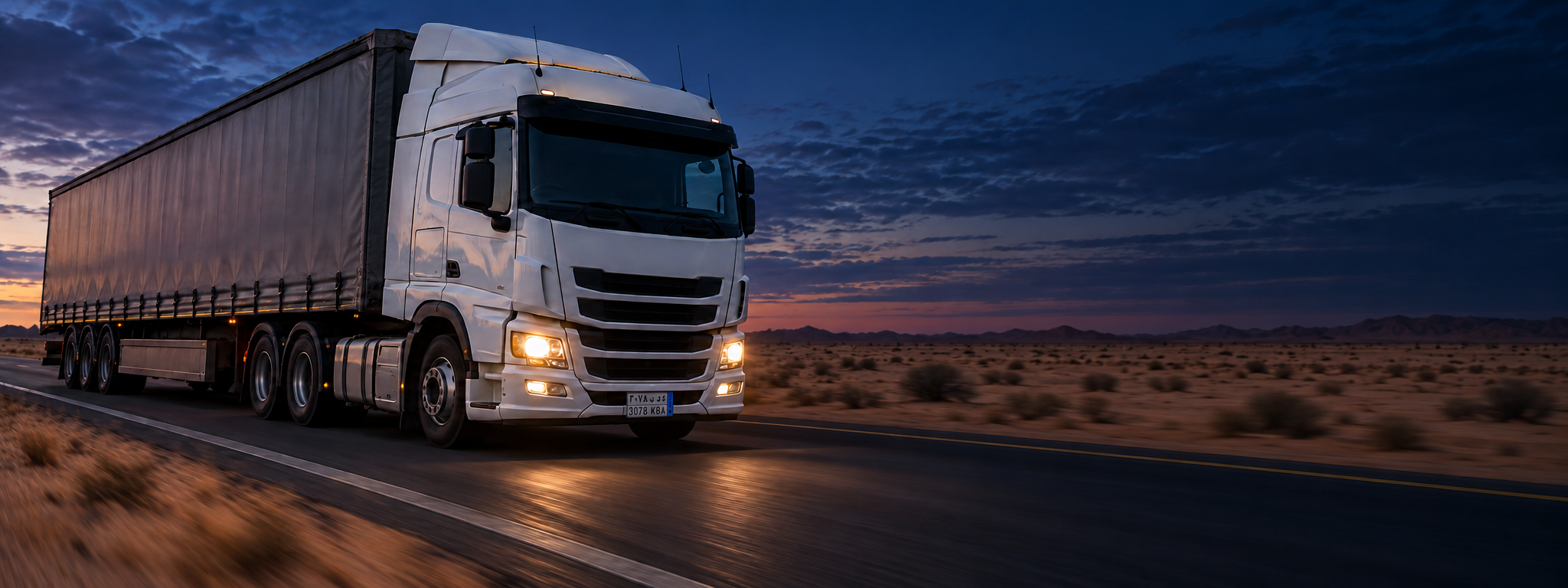 A curtain-sider on a highway at speed, shot from the front three-quarter with motion blur behind. Dark and cool enough for a panel to sit over the right third. No text in the artwork. 2400x900.