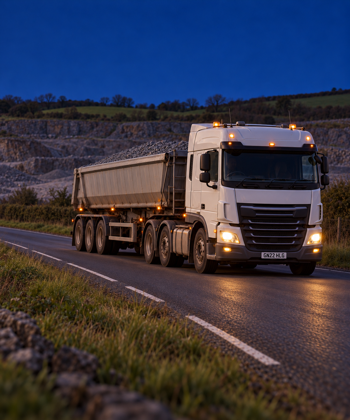 Photograph: a road train on a remote highway at dusk. Dark and cool, room at the top, no text in the artwork.