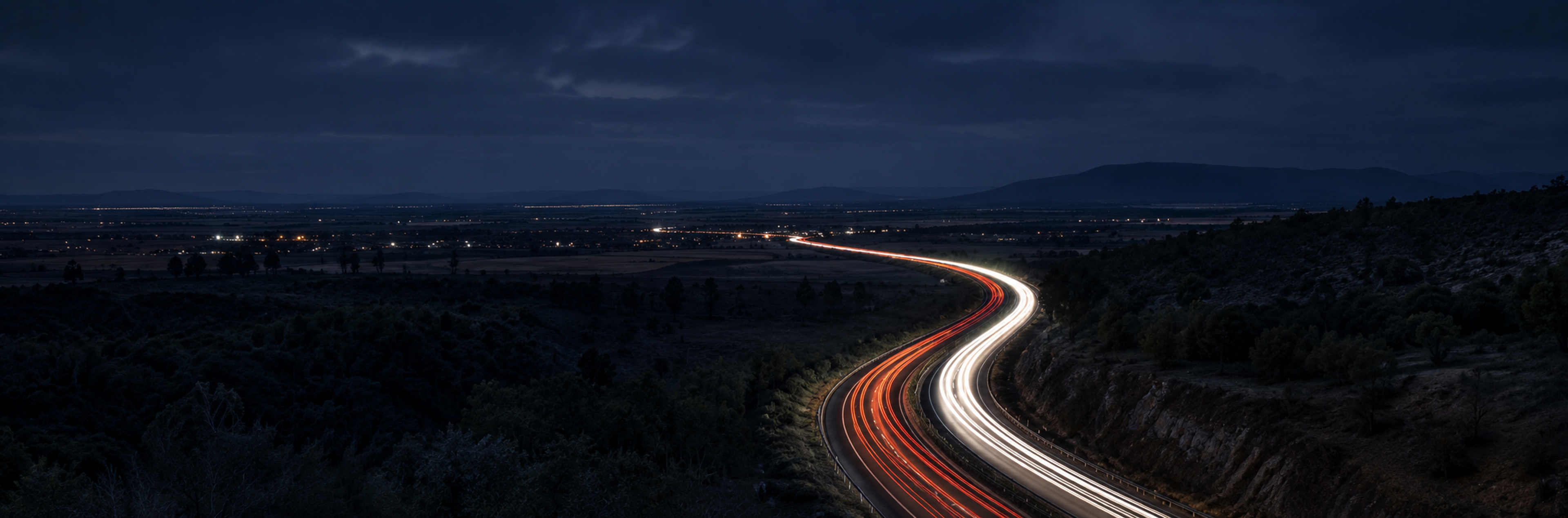 Full-bleed scene, edge to edge: a long highway curve shot from height at dusk, dark and cool so the headline and the accordion read over it. No text in the artwork. 2400x1400.
